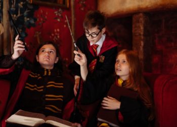 boys and girl in black cloaks holding magic wands